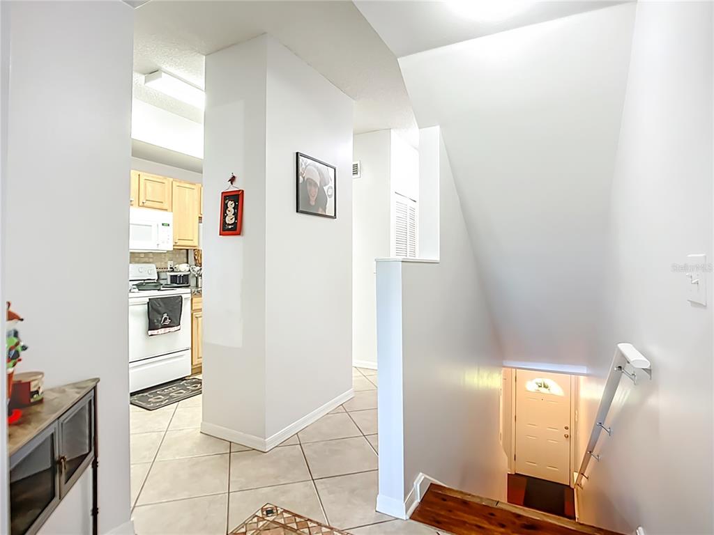 An interior view shows a tiled entryway, a kitchen, and a staircase leading to a door — 4990 BARALDI CIRCLE UNIT 209, SARASOTA, FL
