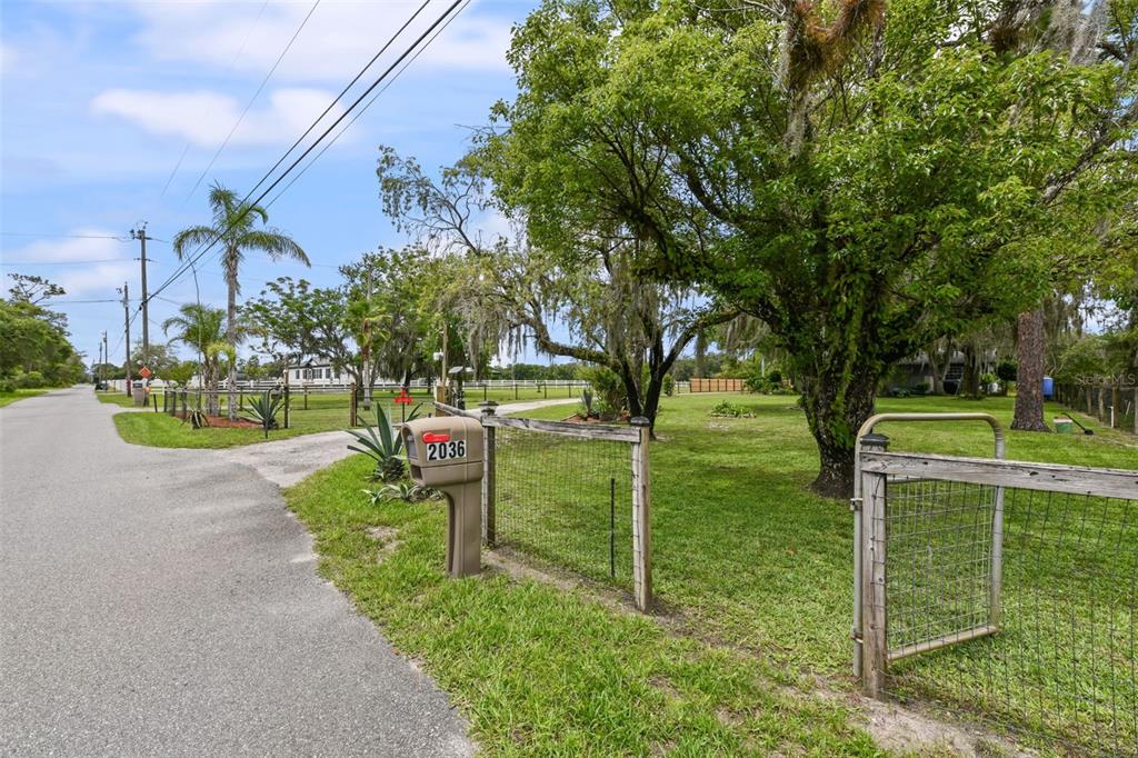 A mailbox labeled 2036 stands beside a wire fence and gate on a grassy lot — 2036 LAKE VIEW AVENUE, CHULUOTA, FL