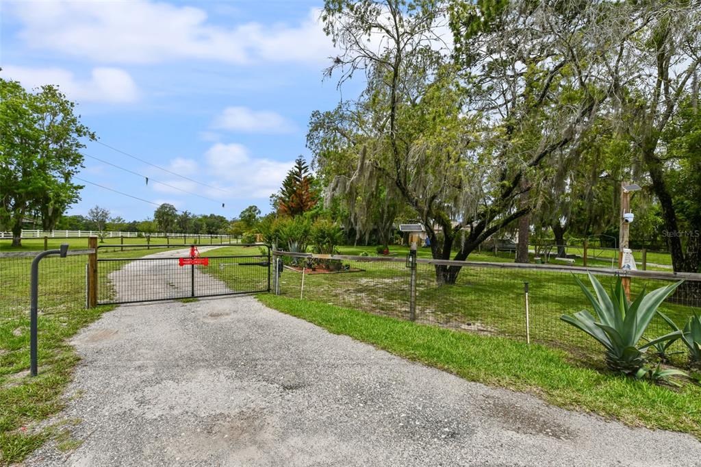 A gravel driveway leads to a gated entrance on a grassy property with mature trees — 2036 LAKE VIEW AVENUE, CHULUOTA, FL
