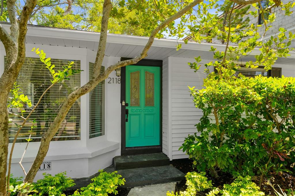 A white house exterior features a bright teal front door with glass panels and landscaping — 2118 S VENUS STREET, TAMPA, FL