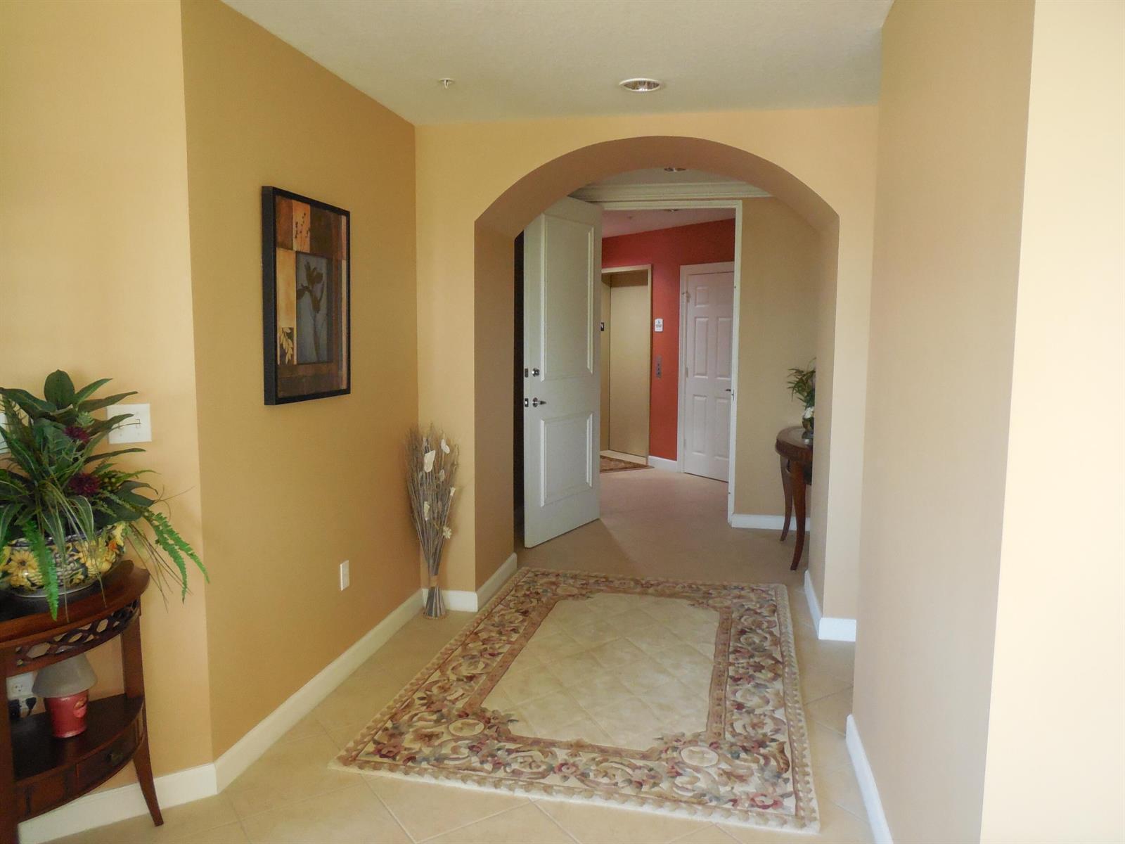A tiled entryway features an arched doorway leading to a carpeted hallway with beige walls — 800 Juno Ocean Walk # 302a, Juno Beach FL 33408, JUNO BEACH, FL