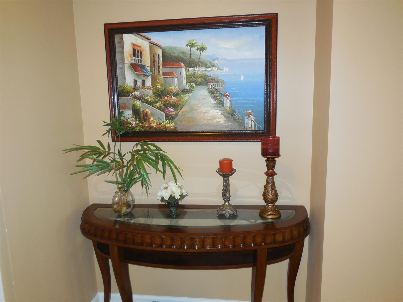 A wooden console table with a glass top sits beneath a framed coastal landscape painting — 800 Juno Ocean Walk # 302a, Juno Beach FL 33408, JUNO BEACH, FL