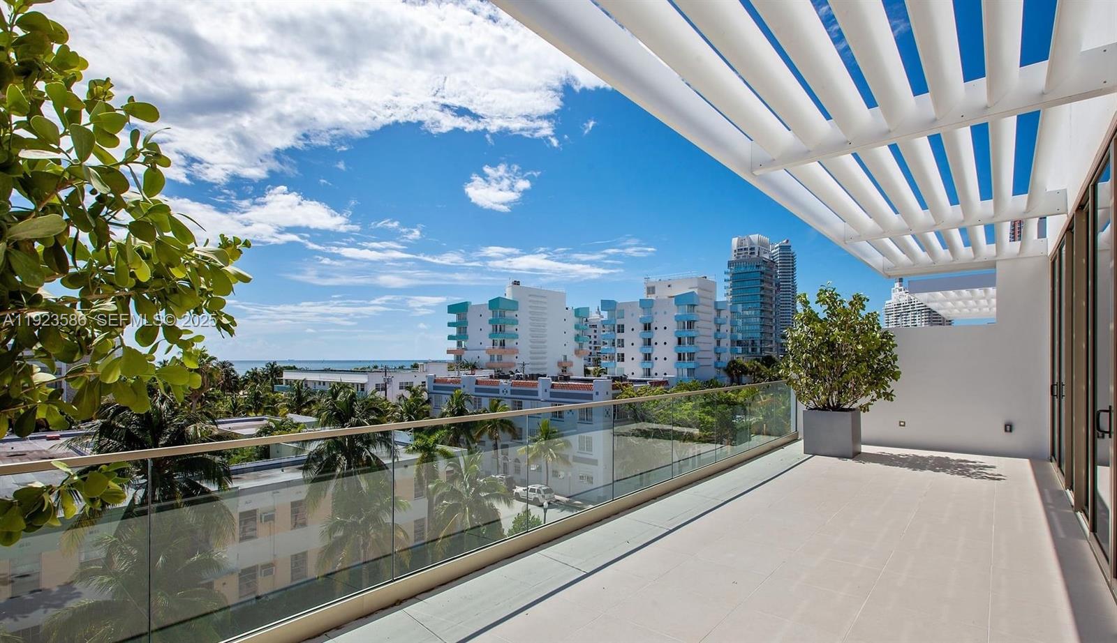 A spacious balcony features a glass railing, a white pergola, and views of nearby buildings — 300 Collins Ave, Miami Beach FL 33139, MIAMI BEACH, FL