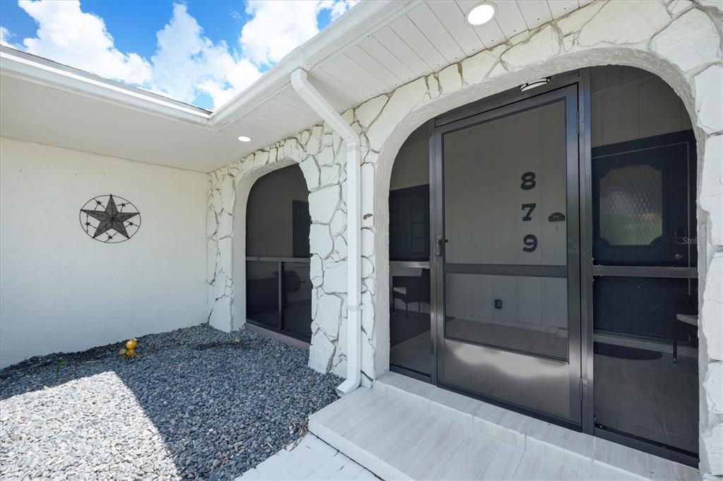 A stone-accented exterior entryway features a screen door, a gravel bed, and a metal star — 879 E 2ND STREET, ENGLEWOOD, FL