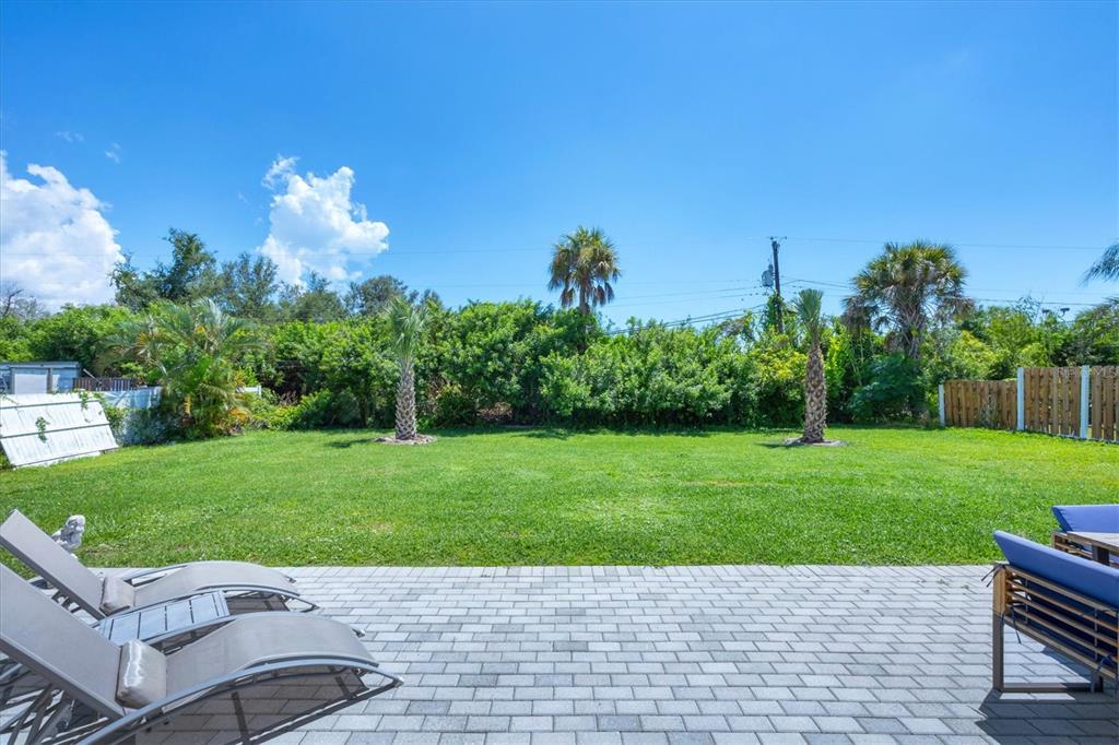 A backyard with a paved patio, lounge chairs, a grassy lawn, and surrounding trees — 879 E 2ND STREET, ENGLEWOOD, FL