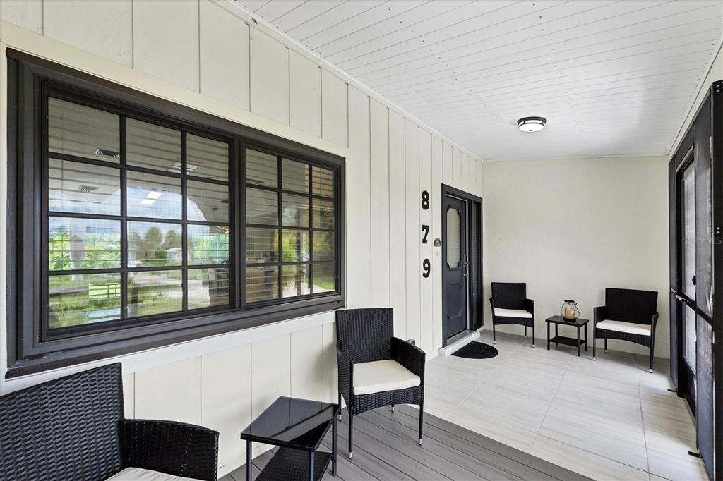 A covered porch features light-colored walls, a dark door, and several black wicker chairs — 879 E 2ND STREET, ENGLEWOOD, FL