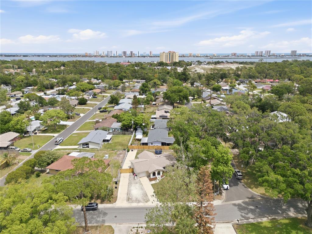 An aerial view shows a suburban neighborhood with houses, trees, and a distant waterfront skyline — 2861 W OAK LEA DRIVE, SOUTH DAYTONA, FL