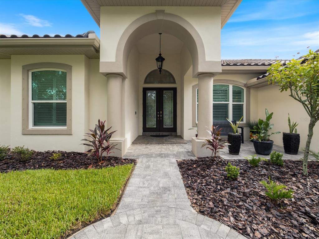 A paved walkway leads to the arched entryway of a house with a double front door — 4987 CROSS POINTE DRIVE, OLDSMAR, FL