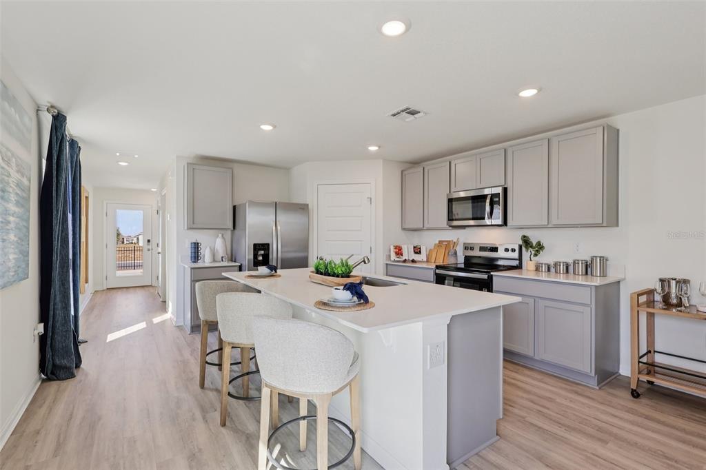 A modern kitchen features gray cabinetry, a white quartz island with bar seating, and light flooring — 5351 CLOUDBERRY AVENUE, LAKELAND, FL