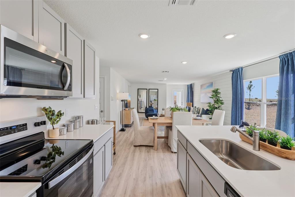 A kitchen with light gray cabinets and white countertops overlooks a dining and living area — 5351 CLOUDBERRY AVENUE, LAKELAND, FL