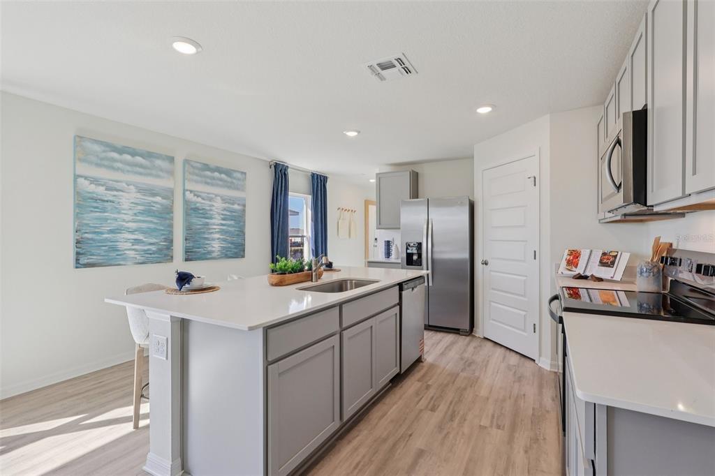 A modern kitchen features a large gray island, stainless steel appliances, and light wood flooring — 5351 CLOUDBERRY AVENUE, LAKELAND, FL