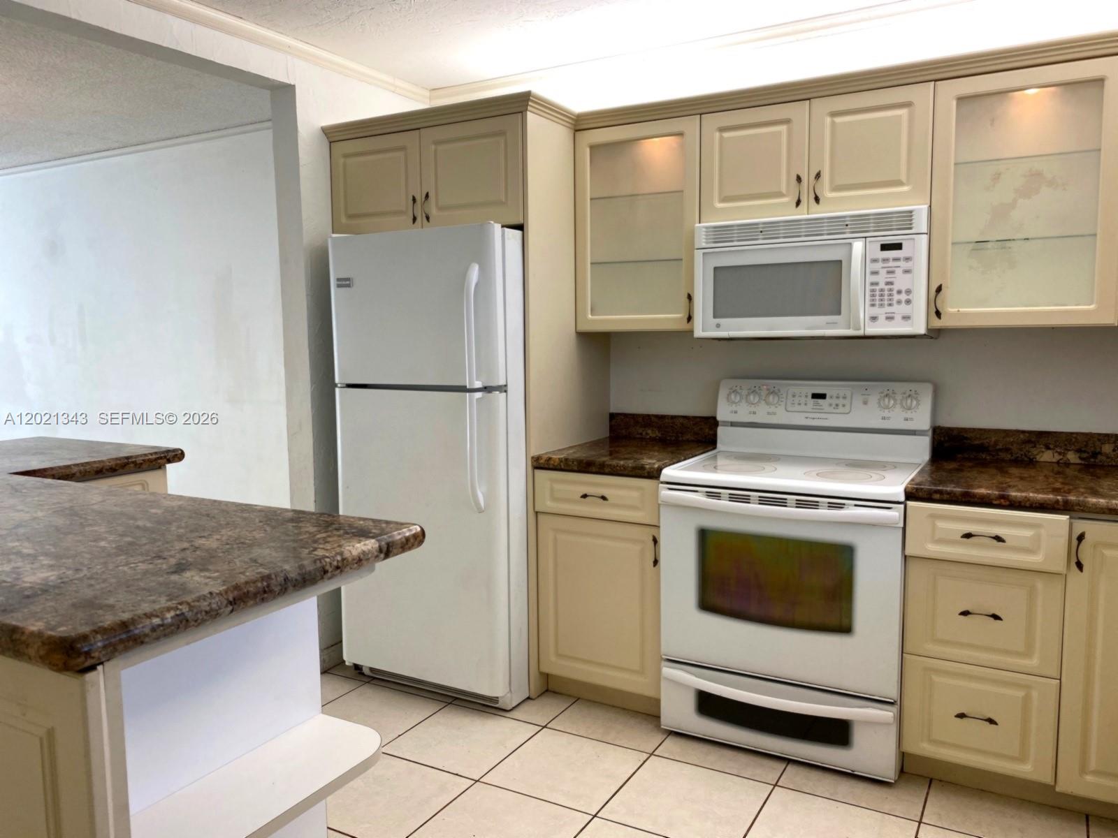 A kitchen features beige cabinets, white appliances, and brown laminate countertops over tiled flooring — 2832 Fillmore St # 22, Hollywood FL 33020, HOLLYWOOD, FL