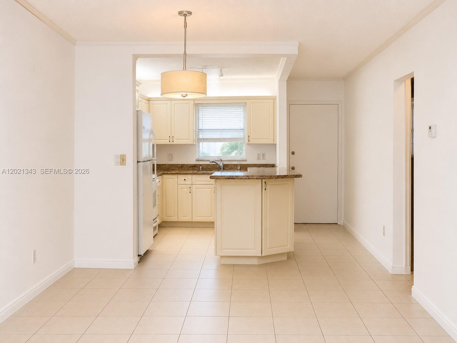 A kitchen features cream cabinets, granite countertops, a central island, and light-colored tile flooring — 2832 Fillmore St # 22, Hollywood FL 33020, HOLLYWOOD, FL