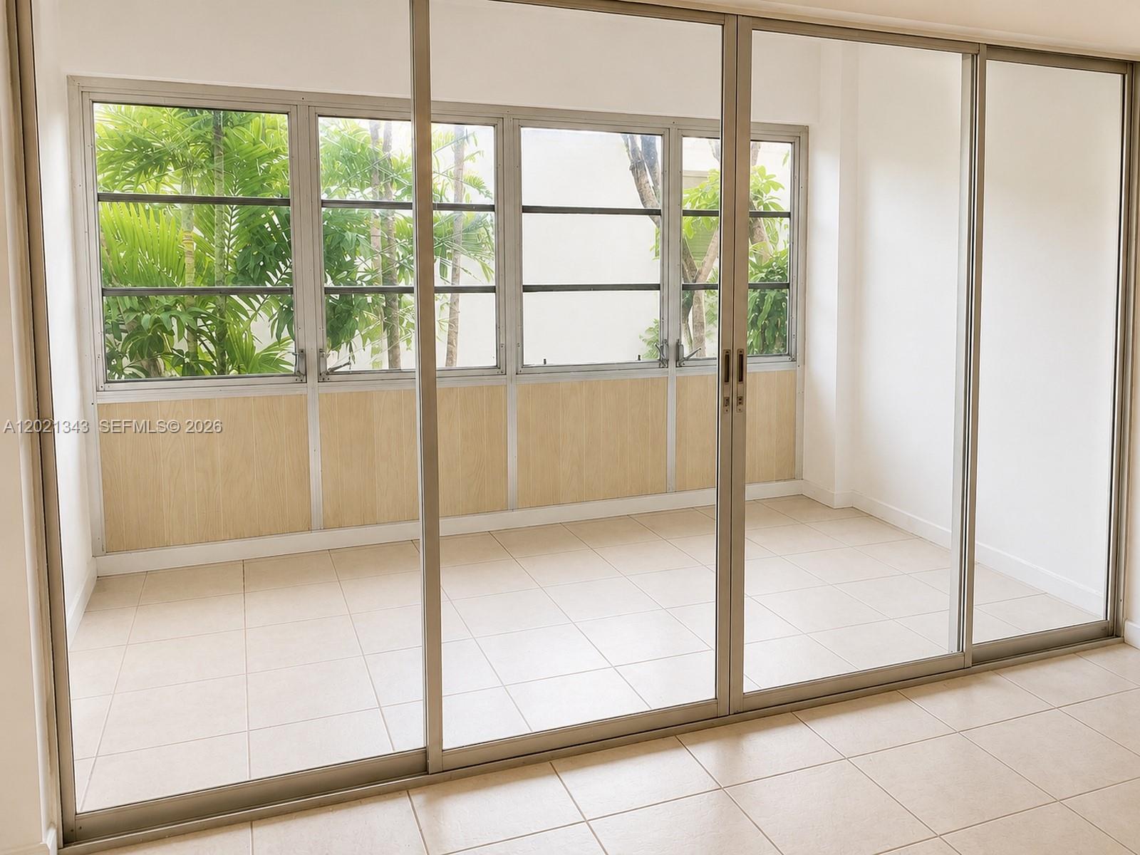 A sunroom with tiled floors, sliding glass doors, and windows overlooking palm trees — 2832 Fillmore St # 22, Hollywood FL 33020, HOLLYWOOD, FL