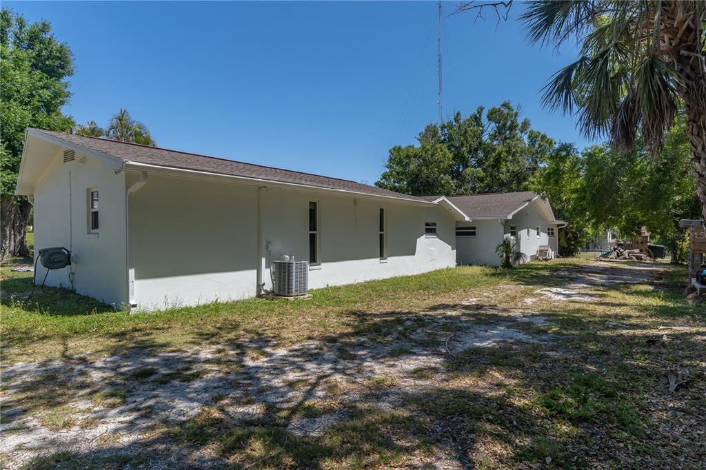 The exterior side view of a white house features a gravel yard and an AC unit — 12705 PARK BOULEVARD, SEMINOLE, FL