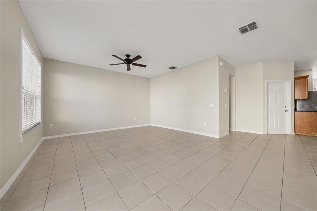 A spacious, empty living room features light-colored tile flooring, beige walls, and a ceiling fan — 3606 SANCTUARY DRIVE, ST CLOUD, FL