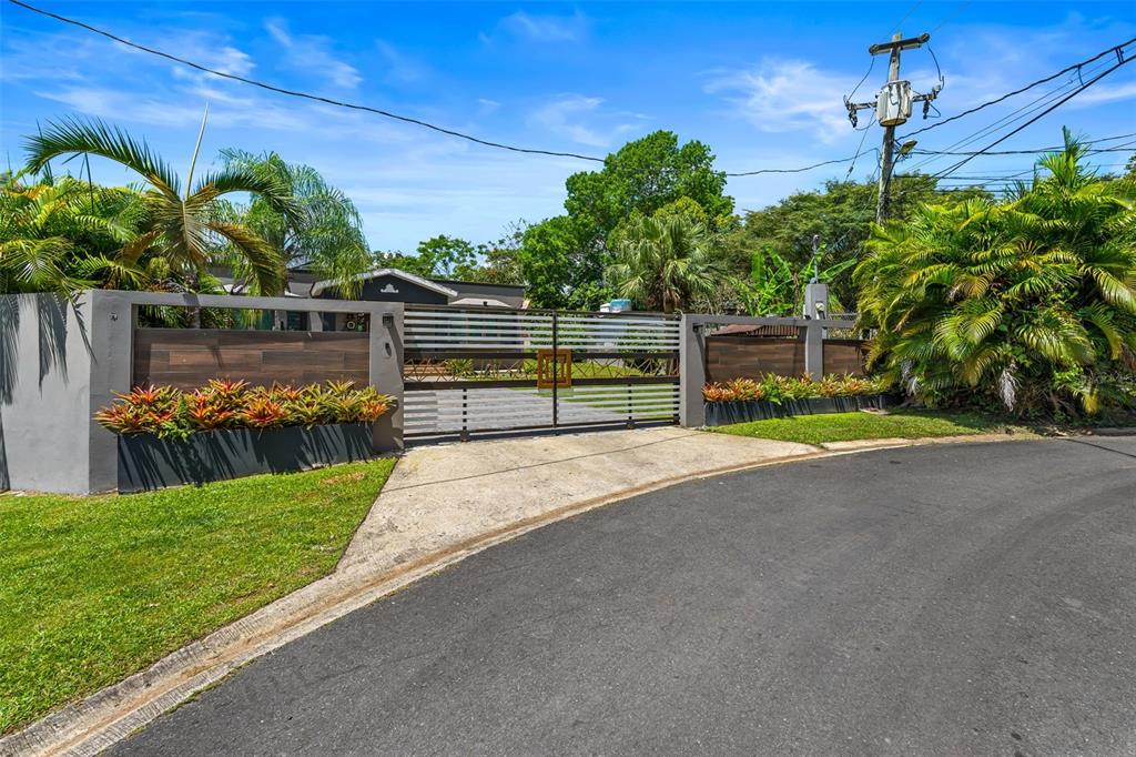 A gated driveway entrance features a modern fence with wood panels and tropical landscaping — Carr 189 Km 16.9 BO CEIBA SUR, JUNCOS, PR