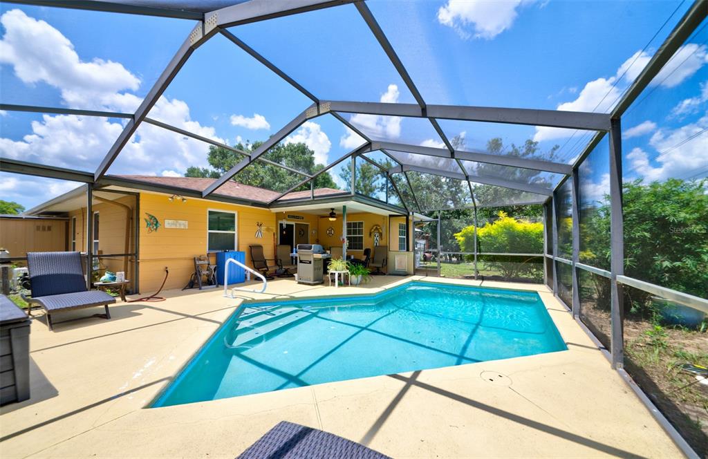 A screened-in patio features a swimming pool, tan concrete decking, and a yellow house exterior — 4441 CHAMBER COURT, SPRING HILL, FL