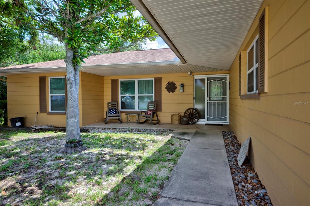 A yellow house exterior features a concrete walkway leading to a covered front porch — 4441 CHAMBER COURT, SPRING HILL, FL