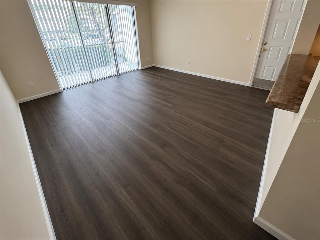 An empty living room features dark wood-look flooring, beige walls, and a sliding glass door — 1612 S PINE RIDGE CIRCLE UNIT 1612, SANFORD, FL