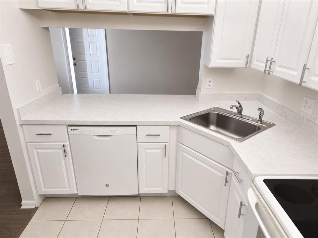 A white kitchen features a dishwasher, stainless steel sink, and white cabinets with laminate countertops — 1612 S PINE RIDGE CIRCLE UNIT 1612, SANFORD, FL