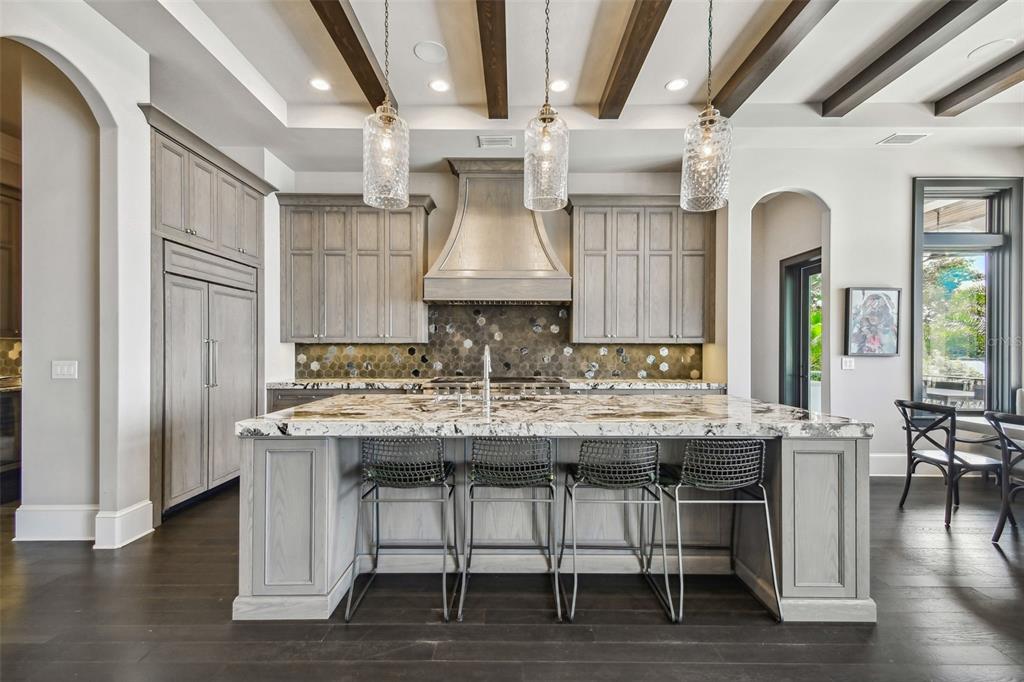 A kitchen features gray cabinetry, a large marble-topped island, and three glass pendant lights — 5120 W LONGFELLOW AVENUE, TAMPA, FL
