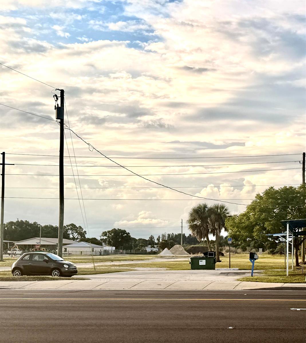 A small car is parked on a paved lot near a dumpster and palm trees — 710 NW Park Street, Okeechobee FL 34972, OKEECHOBEE, FL