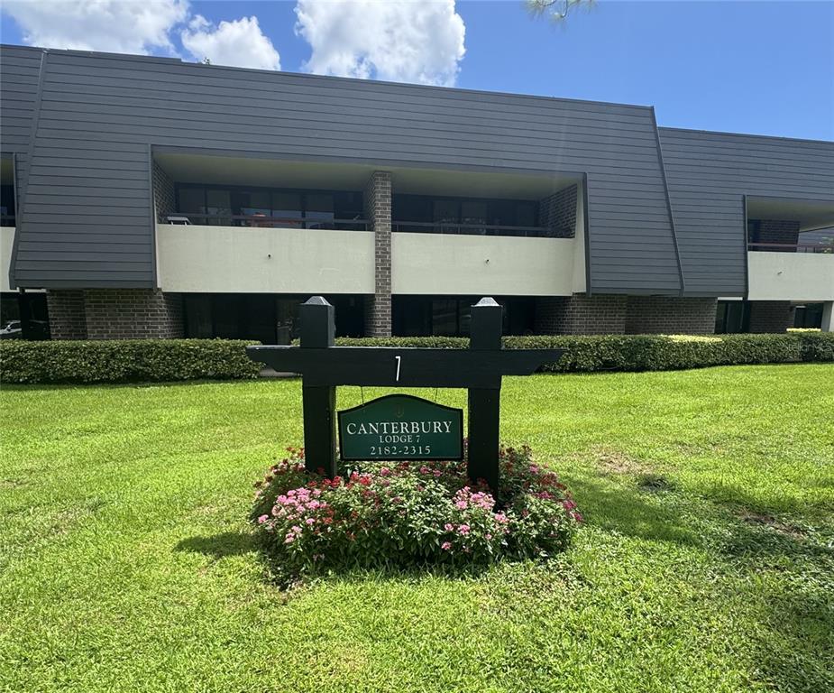 A sign for Canterbury Lodge 7 stands in front of a two-story apartment building — 36750 US HIGHWAY 19 N UNIT 4-209, PALM HARBOR, FL