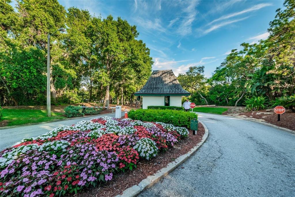 A gated entrance features a guardhouse, a flower bed, and a paved road — 36750 US HIGHWAY 19 N UNIT 4-209, PALM HARBOR, FL