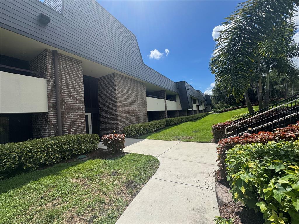 A multi-story brick and gray siding apartment building with a concrete walkway and landscaping — 36750 US HIGHWAY 19 N UNIT 4-209, PALM HARBOR, FL