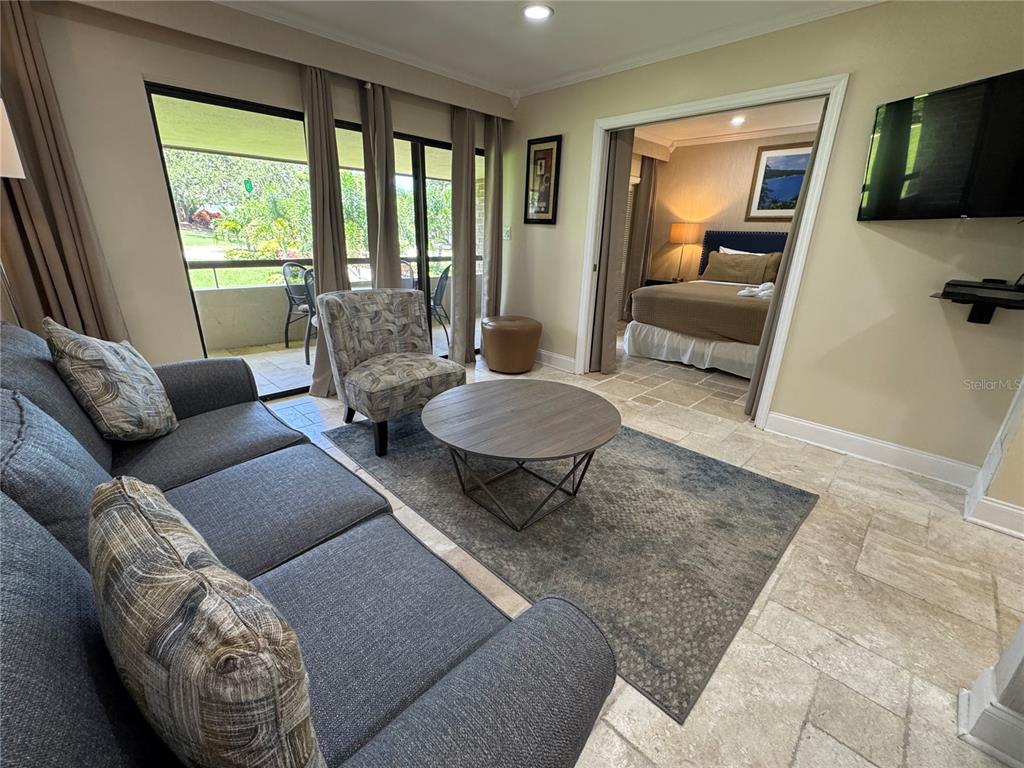 A living room with a gray sofa and coffee table opens into a bedroom — 36750 US HIGHWAY 19 N UNIT 4-209, PALM HARBOR, FL