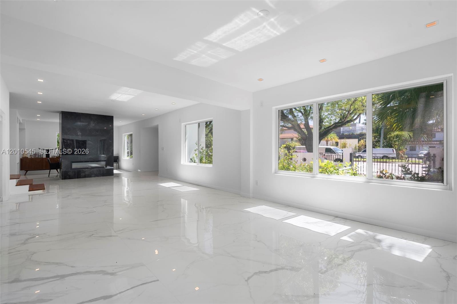 A bright, open living room features white marble floors, a black stone fireplace, and large windows — 5824 Alton Rd, Miami Beach FL 33140, MIAMI BEACH, FL