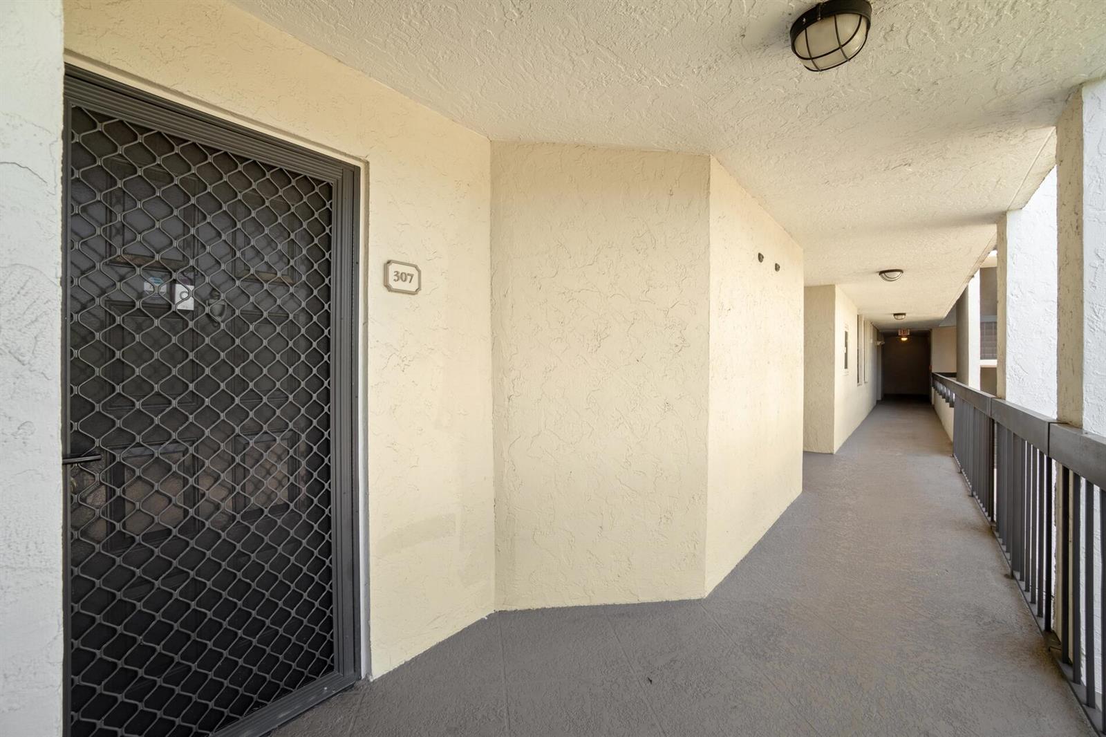An outdoor apartment hallway features a unit door with a security screen and metal railings — 950 Lavers Circle # F307, Delray Beach FL 33444, DELRAY BEACH, FL