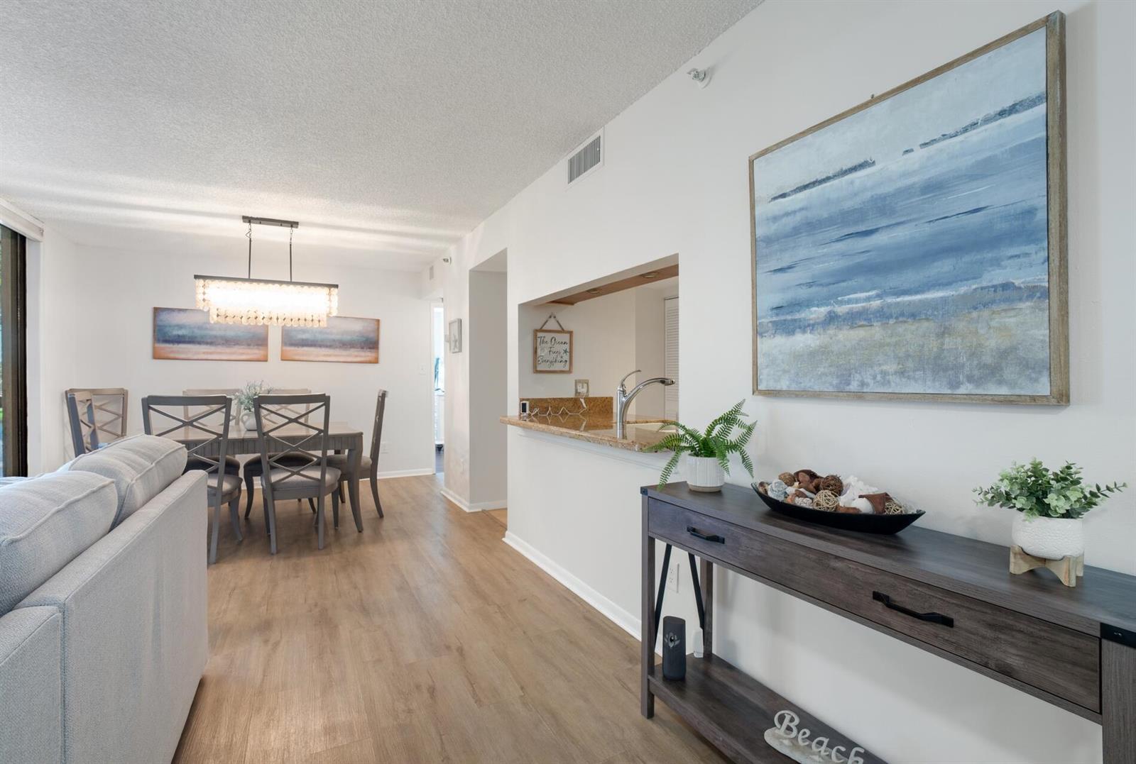 A living room and dining area feature light wood flooring, white walls, and coastal decor — 950 Lavers Circle # F307, Delray Beach FL 33444, DELRAY BEACH, FL