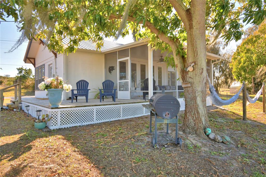A house exterior features a wooden deck with blue chairs, a screened porch, and grill — 1173 S LAKE REEDY BOULEVARD, FROSTPROOF, FL