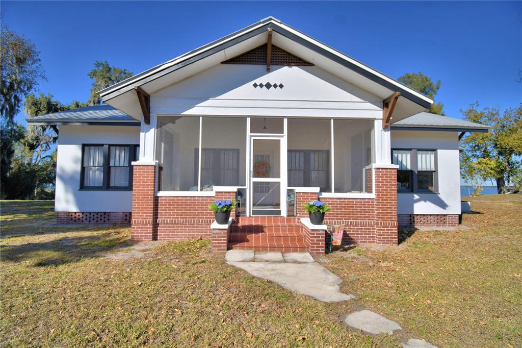 A white house with a brick-based screened porch stands on a grassy lot — 1173 S LAKE REEDY BOULEVARD, FROSTPROOF, FL