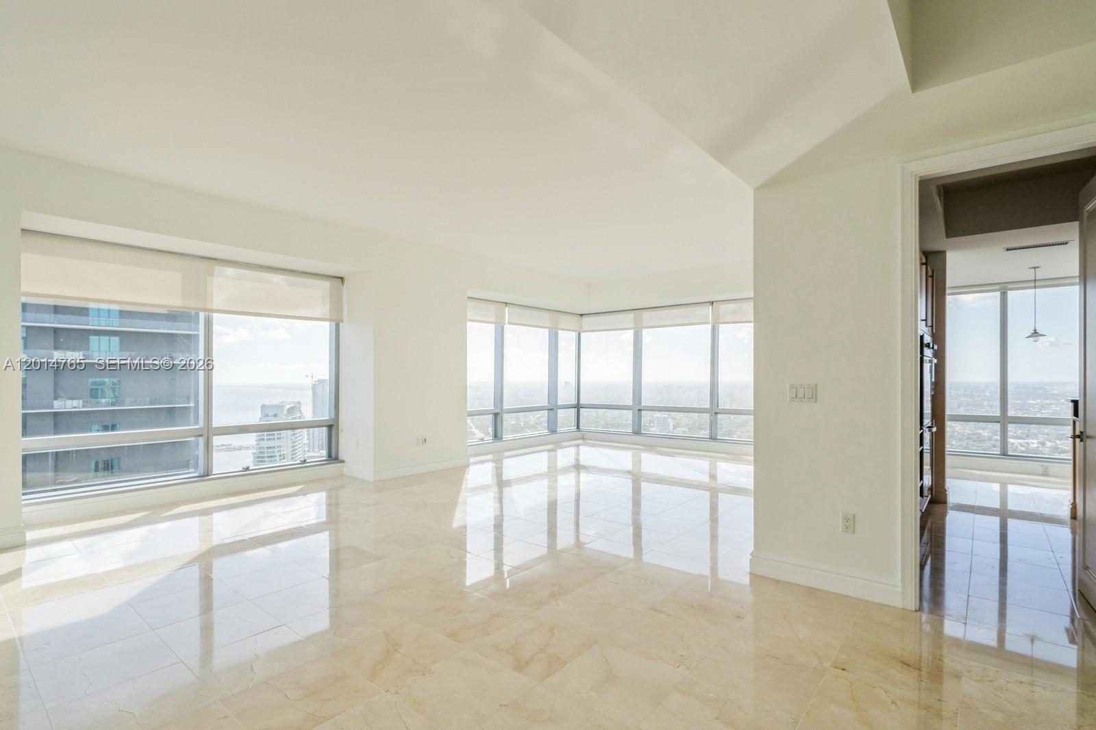 An empty room with light-colored tile floors and floor-to-ceiling windows overlooking a city skyline — 1425 Brickell Ave # 57B, Miami FL 33131, MIAMI, FL