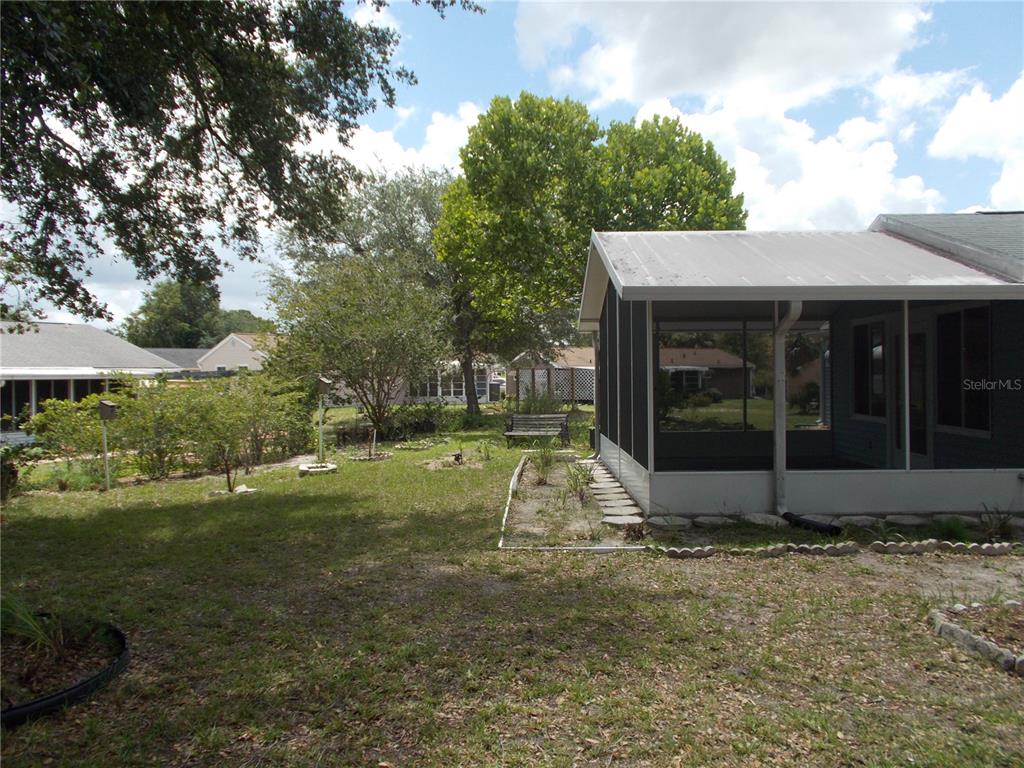 A backyard view featuring a screened-in porch, a grassy lawn, and mature trees — 10877 SW 88TH COURT, OCALA, FL