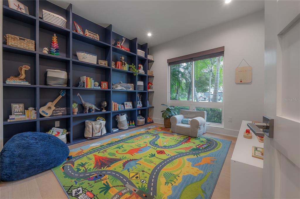 A child's playroom features a large blue built-in bookshelf, a dinosaur-themed rug, and a window — 4207 W JETTON AVENUE, TAMPA, FL