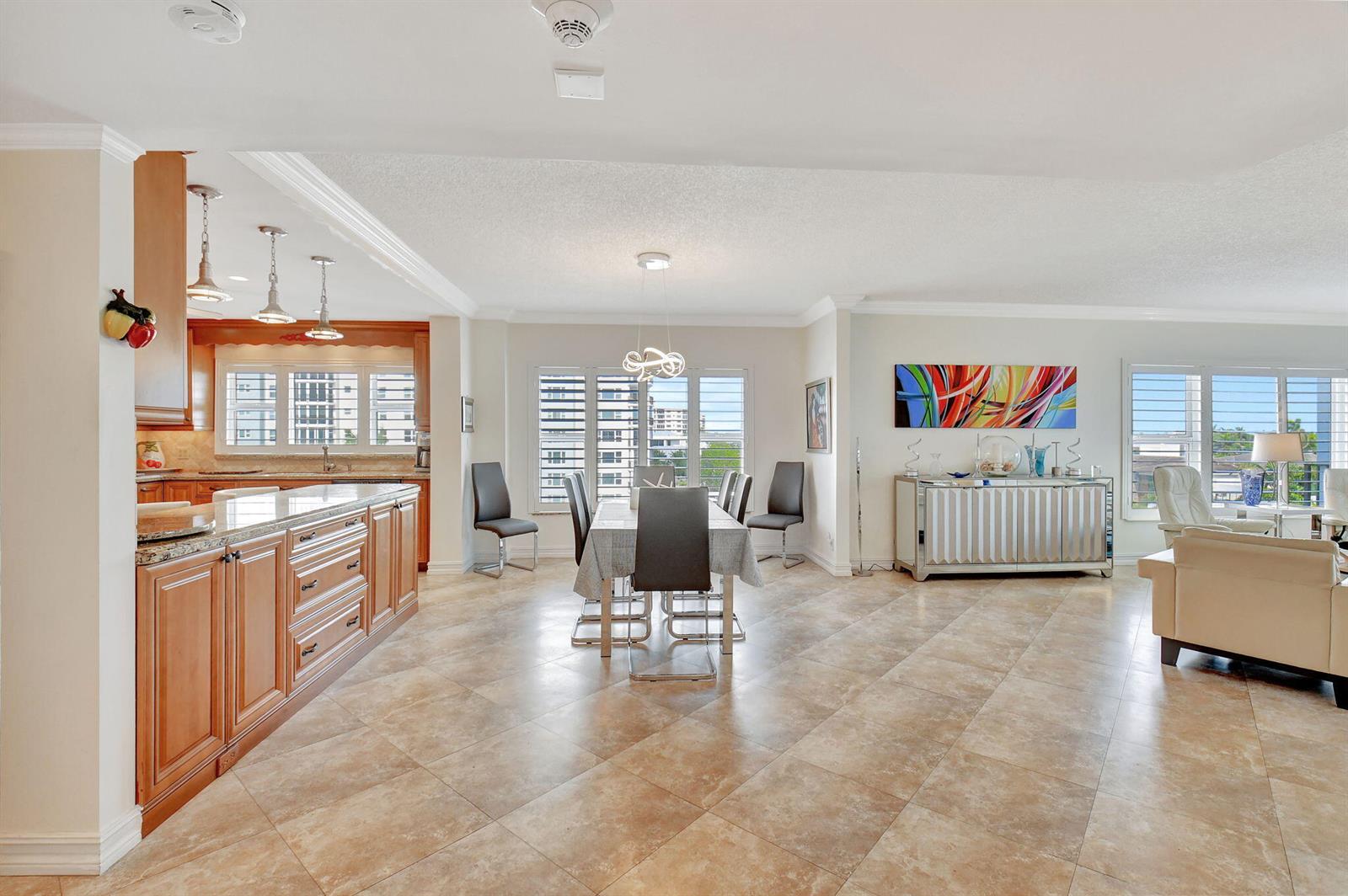 An open-concept kitchen and dining area features wood cabinets, tile flooring, and large windows — 220 Macfarlane Drive # 505, Delray Beach FL 33483, DELRAY BEACH, FL