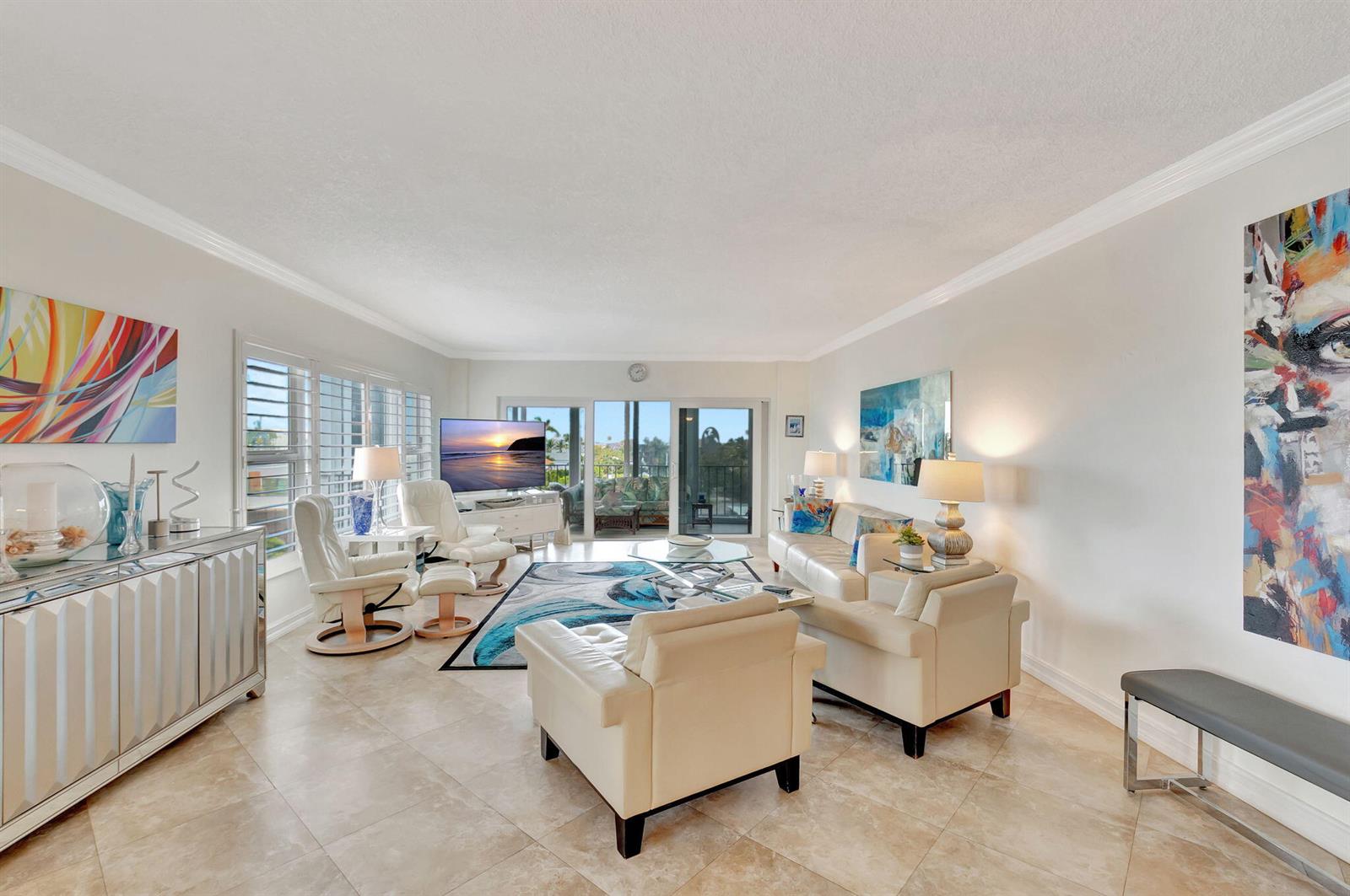 A bright living room features light tile floors, white leather furniture, and colorful abstract wall art — 220 Macfarlane Drive # 505, Delray Beach FL 33483, DELRAY BEACH, FL