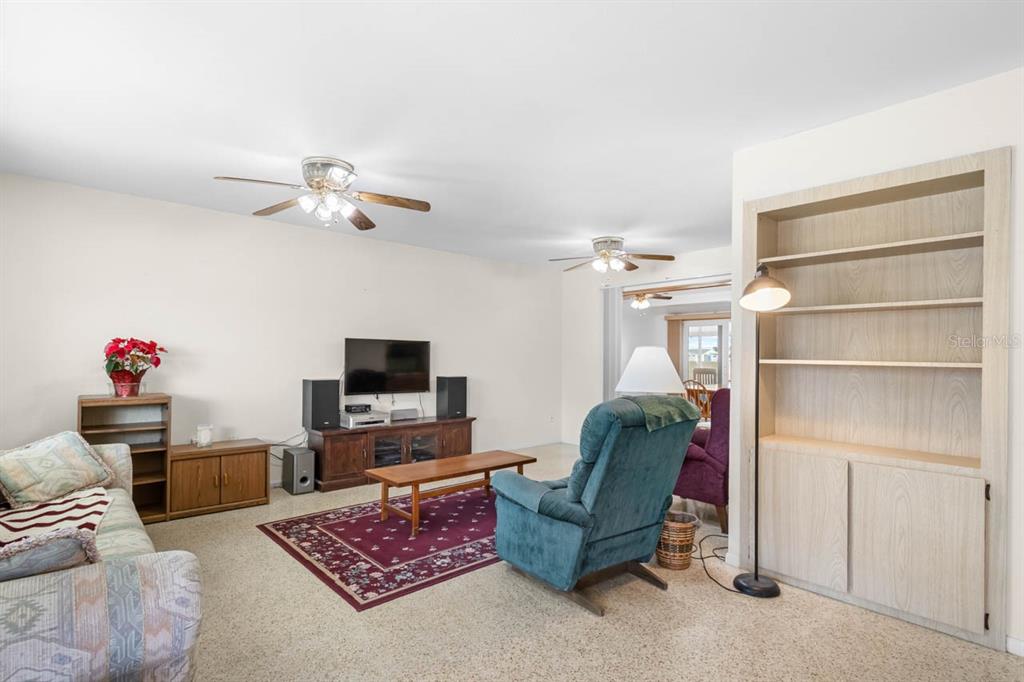 A living room features a television console, a teal recliner, and a built-in wooden bookshelf — 1001 AUGUSTA DRIVE, SUN CITY CENTER, FL