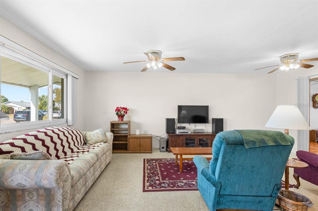 A living room with a patterned sofa, blue recliner, television console, and two ceiling fans — 1001 AUGUSTA DRIVE, SUN CITY CENTER, FL