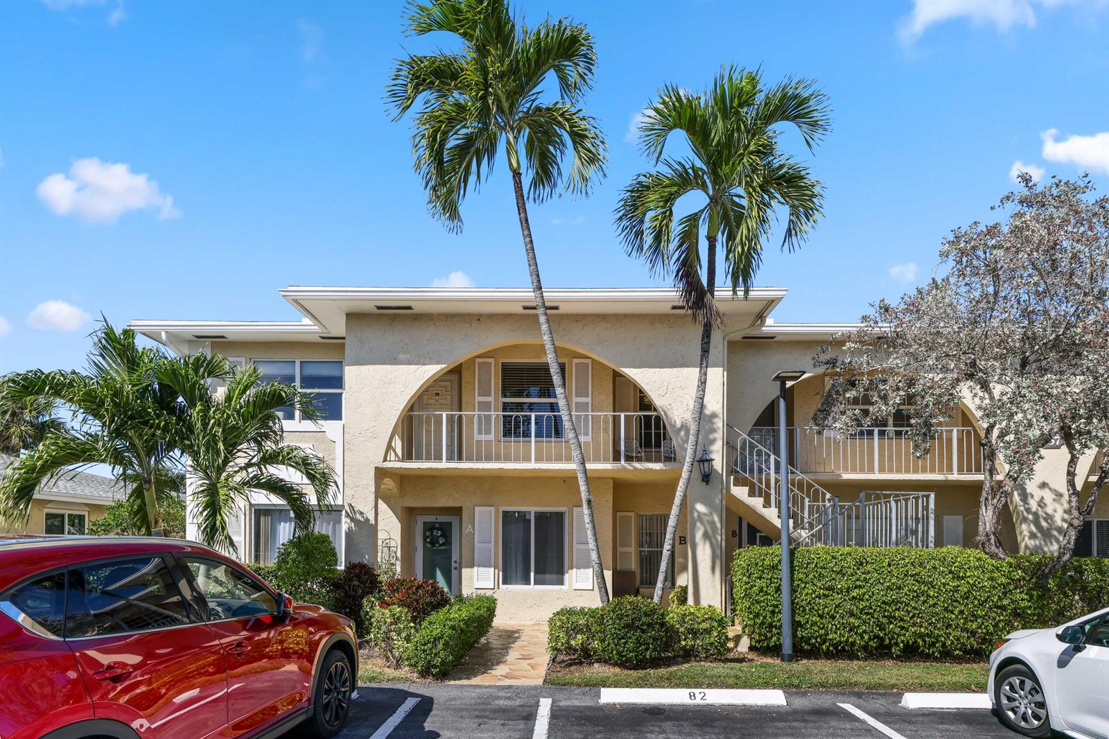 A two-story apartment building with a central arched balcony and palm trees in front — 13757 Flora Place, Delray Beach FL 33484, DELRAY BEACH, FL