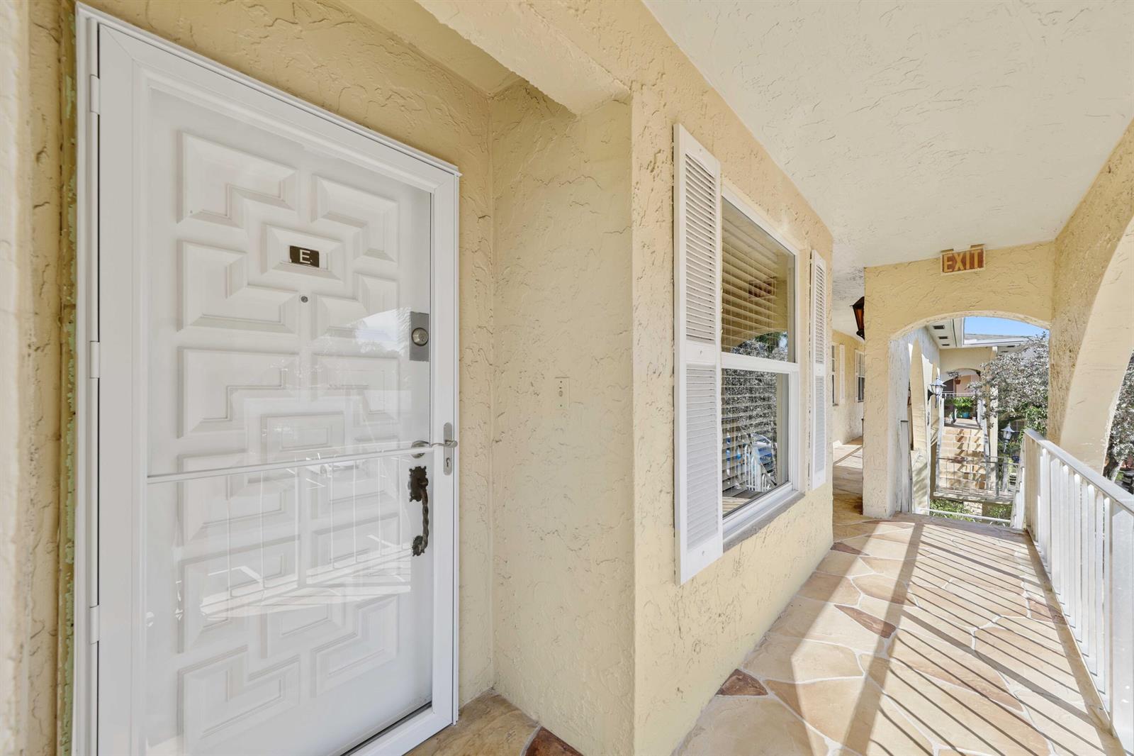 A white door with a letter E sign opens onto a tiled outdoor walkway — 13757 Flora Place, Delray Beach FL 33484, DELRAY BEACH, FL