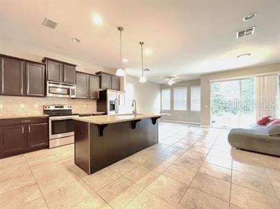 A kitchen with dark cabinets, a center island, and tile flooring opens to a living area — 1445 PETERSON PLACE, SANFORD, FL