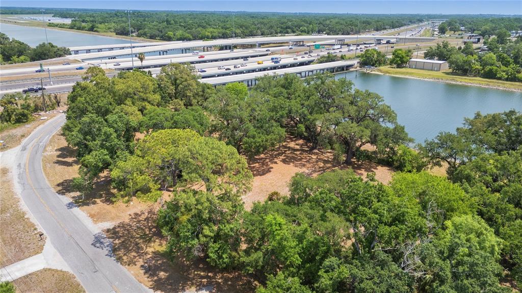 An aerial view shows a wooded lot adjacent to a lake and a highway overpass — 5013 GARDEN LANE, TAMPA, FL