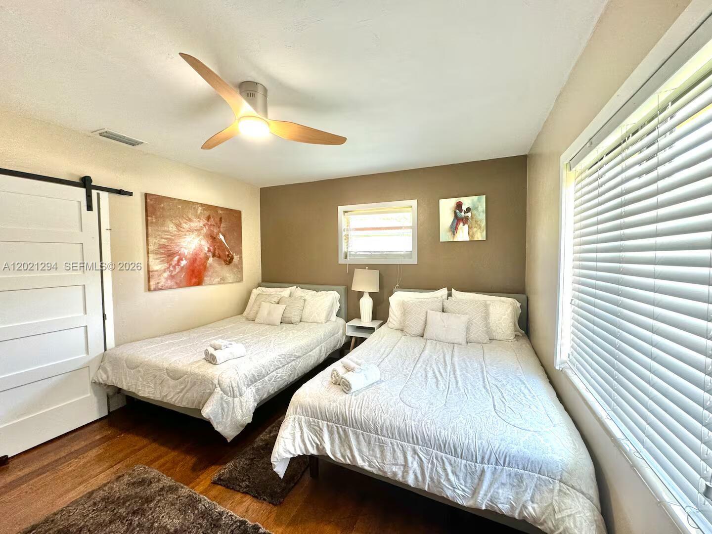 A bedroom features two beds, a ceiling fan, wood flooring, and a barn-style door — 1275 NW 50th St # 0, Miami FL 33142, MIAMI, FL