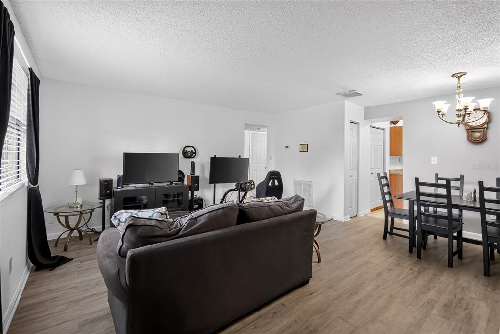 A living room with wood-look flooring, a gray sofa, a television console, and a dining area — 12405 OAK CEDAR PLACE UNIT 202, TAMPA, FL