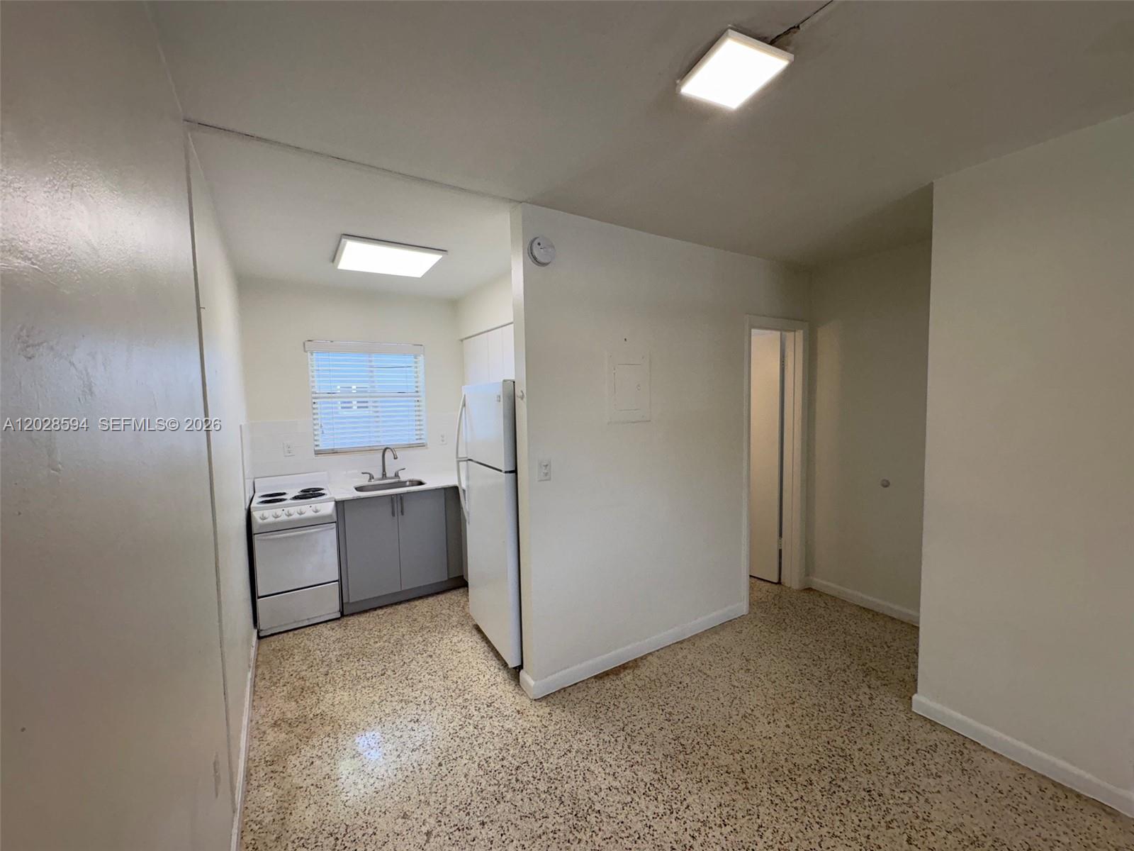 A small kitchen features a white stove, gray cabinets, a refrigerator, and speckled flooring — 320 W 10th St # 3, Hialeah FL 33010, HIALEAH, FL